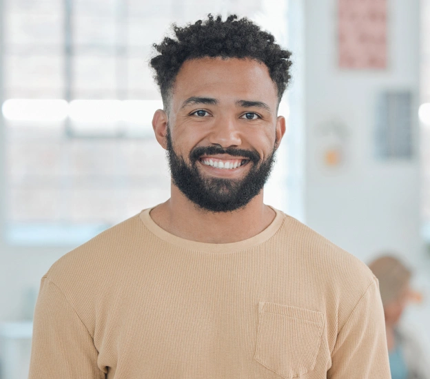 Smiling man wearing tan shirt in bright office setting, professional headshot for dental practice.