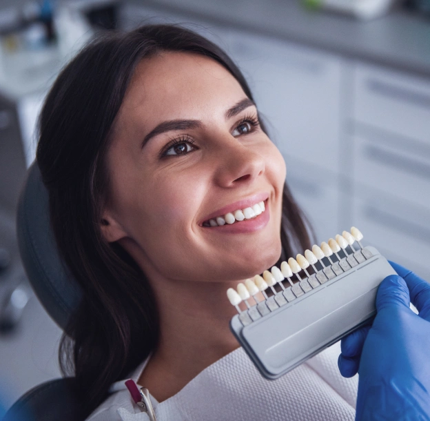 Dental professional holding shade guide in clinical setting, smiling at camera.