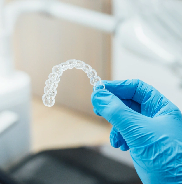 Dentist in blue gloves holding clear plastic aligner or retainer in clinical setting.
