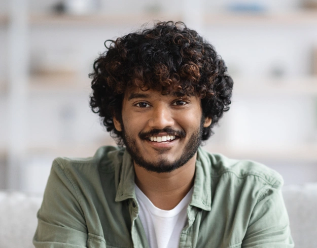 Smiling man with curly dark hair wearing green shirt in bright office setting.