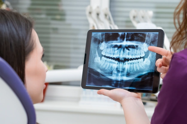 Dentist showing patient dental X-ray on tablet in clinical office setting.