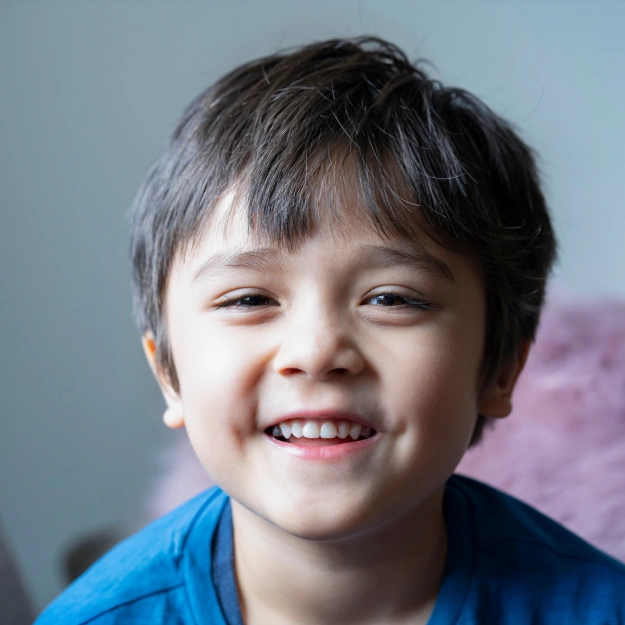 Young boy smiling at camera wearing blue shirt, dental office setting background