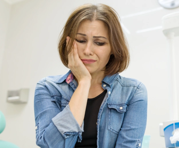 Woman in denim shirt resting head on hand, appearing thoughtful in dental office setting.
