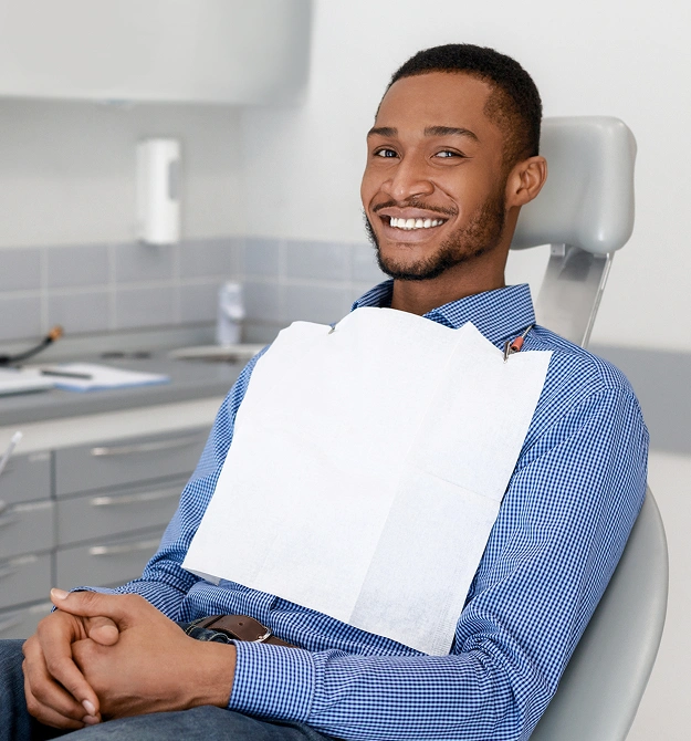 Smiling male patient holding blank clipboard in dental office chair.