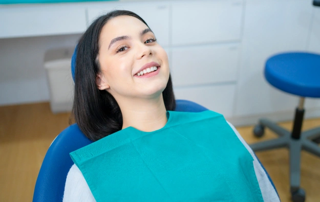 Smiling woman in dental chair wearing turquoise bib at dentist office