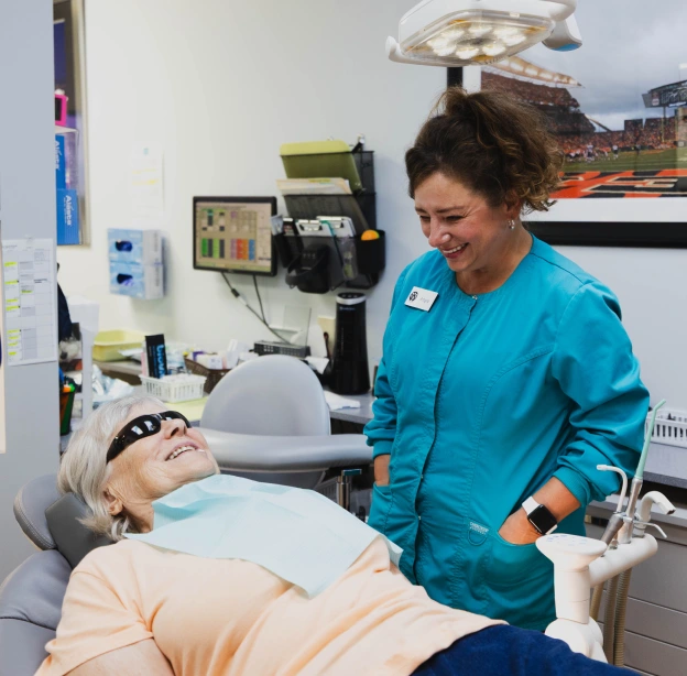 Dental hygienist performing ultrasonic cleaning on patient in modern dental office treatment room.