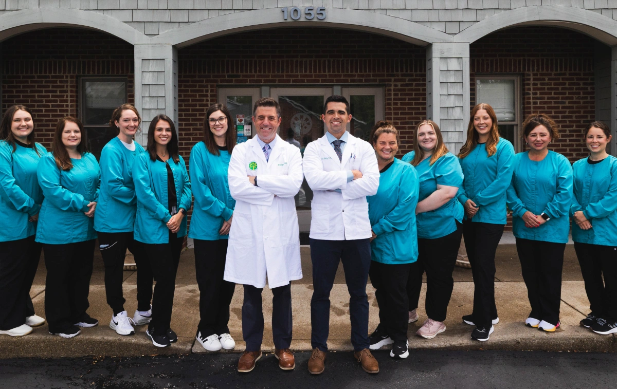 Forest Hills Family Dentistry team of dentists and staff in teal scrubs standing outside brick building.